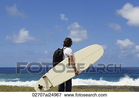 Stock Photo - man holding surf board, facing sea. Fotosearch