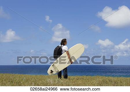 Stock Photograph - man holding surf board, looking out to sea. Fotosearch