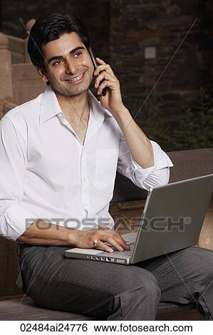 Stock Photograph - man on phone, working on laptop computer. Fotosearch
