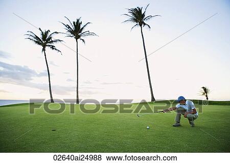 Stock Photo - man squatting on golf course, judging angle. Fotosearch