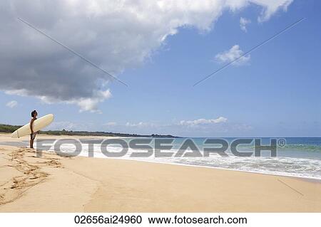 Stock Image - man standing on beach, looking at waves. Fotosearch