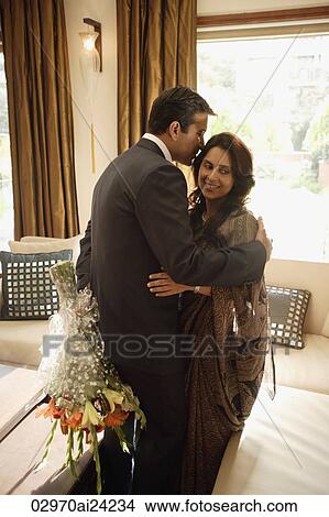 Picture - man whispering in woman's ear, flowers behind his back. Fotosearch
