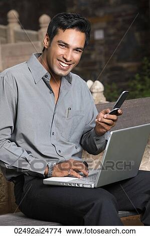 Picture - man with phone and laptop computer. Fotosearch