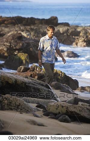 Stock Photo - mature man walking along rocky beach. Fotosearch