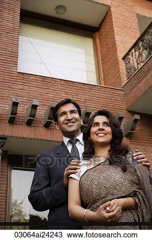 Stock Image - smiling couple, standing in front of home. Fotosearch
