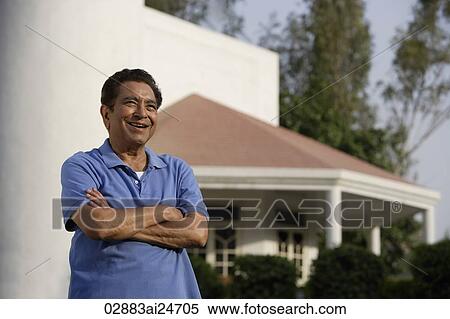 Stock Photography - smiling man standing in front of house, arms crossed. Fotosearch