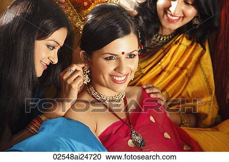 Stock Image - three women in saris, one placing necklace on another. Fotosearch