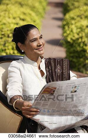 Stock Image - woman reading newspaper, dressed in salwar kameez and shawl. Fotosearch