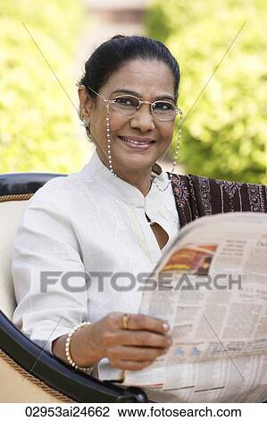 Stock Image - woman reading newspaper, wearing glasses, salwar kameez and shawl. Fotosearch
