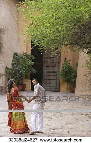 Stock Photo - young couple holding hands, woman in sari, walking in courtyard. Fotosearch