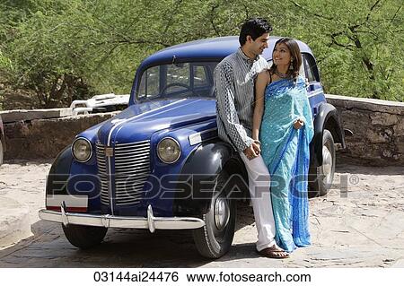 Stock Photograph - young couple looking at each other in front of blue antique car. Fotosearch
