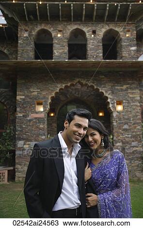 Stock Image - young couple posing in front of home, woman in sari. Fotosearch