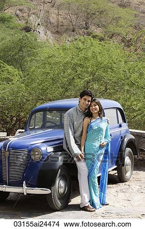 Picture - young couple standing in front of blue antique car. Fotosearch