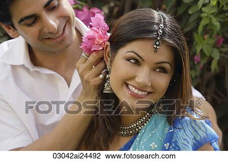 Stock Image - young man putting flowers behind young woman's ear. Fotosearch