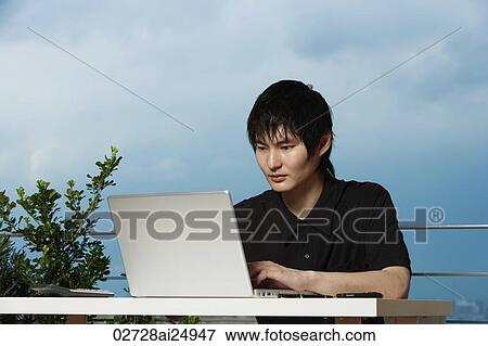 Stock Photo - young man sitting outdoor using laptop. Fotosearch