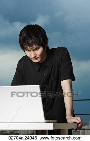 young man standing, using laptop View Large Photo Image Stock Photograph - young man standing, using laptop. Fotosearch