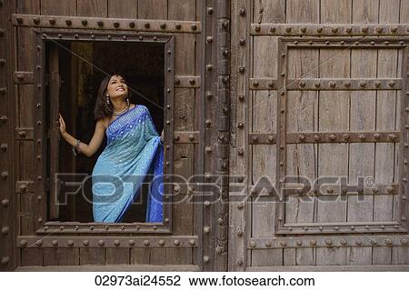 Stock Image - young woman in sari at window inside huge wooden doorway. Fotosearch