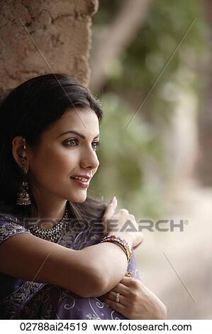 Stock Photo - young woman in sari, sitting smiling arms wrapped around self. Fotosearch