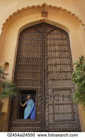 Stock Image - young woman in sari, standing at a huge wooden doorway. Fotosearch