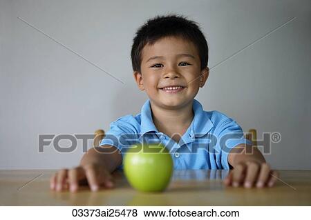Boy sitting at table with green apple View Large Photo Image Stock Photo - Boy sitting at table with green apple. Fotosearch