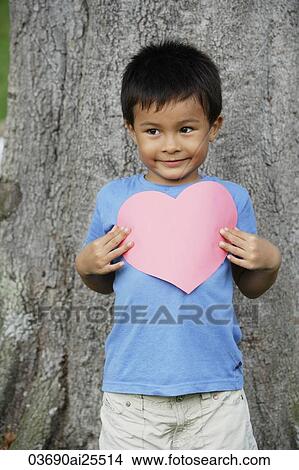 Boy standing by tree holding heart View Large Photo Image Picture - Boy standing by tree holding heart. Fotosearch