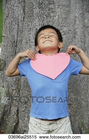 Boy standing by tree holding heart View Large Photo Image Stock Photography - Boy standing by tree holding heart. Fotosearch
