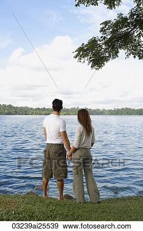 Stock Photo - Couple holding hands looking at lake. Fotosearch