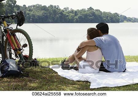 Stock Photo - Couple sitting on blanket by a lake. Fotosearch