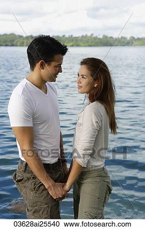 Stock Image - Couple standing hand in hand by lake. Fotosearch