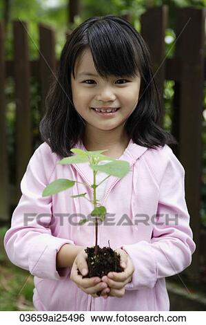 Stock Photograph - Girl holding plant in soil. Fotosearch