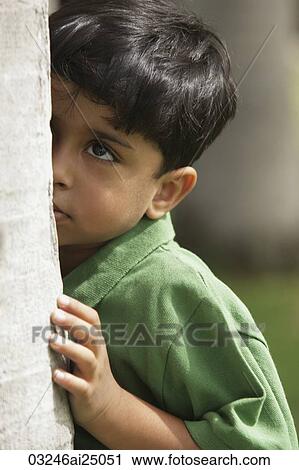 Stock Image - Little boy peaking up side of tree trunk. Fotosearch