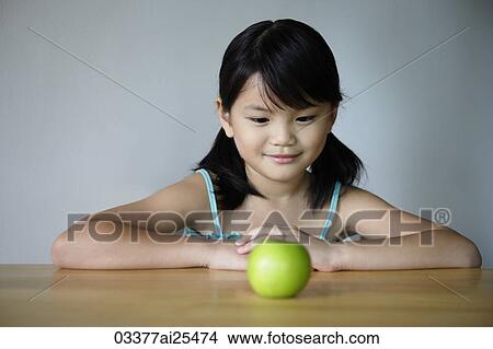 Little girl at table looking at green apple View Large Photo Image Picture - Little girl at table looking at green apple. Fotosearch
