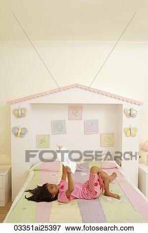 Stock Photo - little girl reading book on bed. Fotosearch