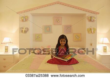 Stock Photo - little girl reading book on bed. Fotosearch