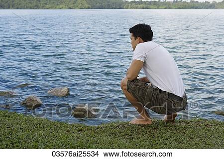 Picture - Man bending down next to lake. Fotosearch
