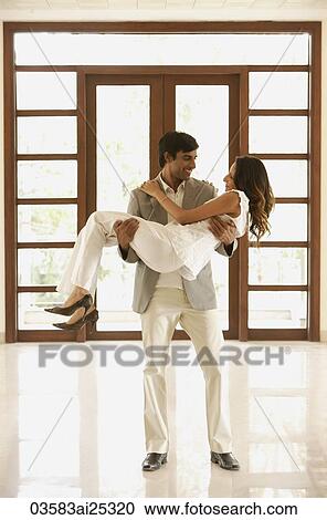 Stock Image - man carrying woman over threshold into empty home. Fotosearch