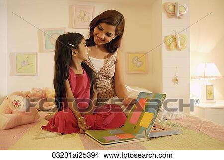 Picture - mother and daughter reading book on bed. Fotosearch