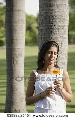 Picture - teen girl leaning against tree, with flower. Fotosearch