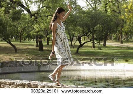 Teen girl walking on wall by lake View Large Photo Image Stock Image - Teen girl walking on wall by lake. Fotosearch