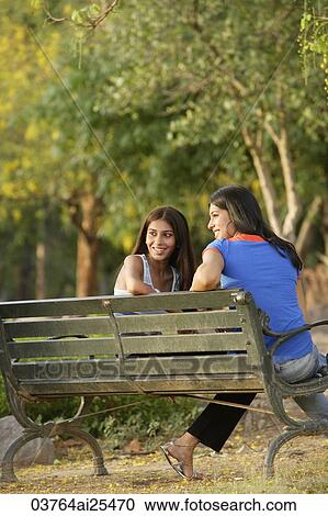 Stock Image - Two teen girls sitting on park bench. Fotosearch