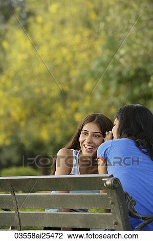 Stock Image - Two teen girls telling secrets in park. Fotosearch