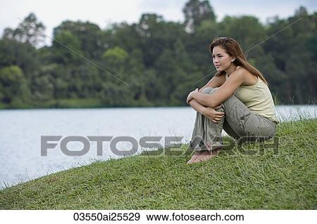 Stock Photo - Woman hugging her knees by lake. Fotosearch