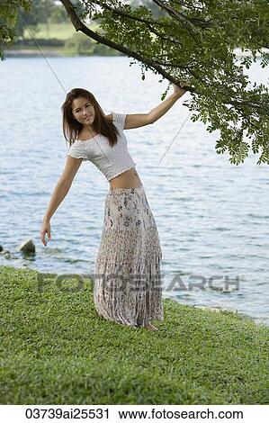 Woman standing under tree near lake View Large Photo Image Stock Image - Woman standing under tree near lake. Fotosearch