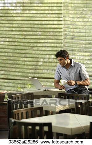 Stock Photograph - young man at laptop, with coffee. Fotosearch