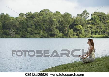Stock Photograph - Young woman meditating beside a lake. Fotosearch
