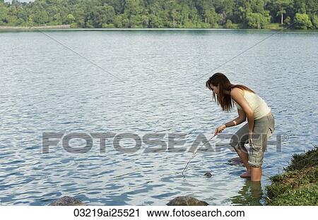 Stock Image - Young woman playing with stick in lake. Fotosearch