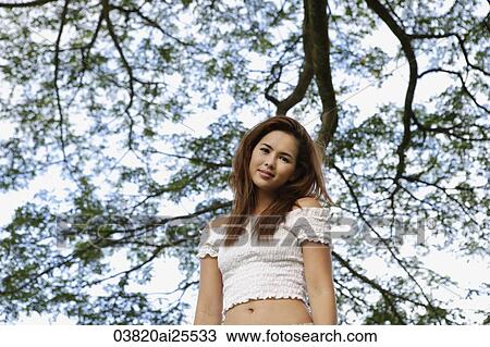 Young woman standing under tree View Large Photo Image Stock Image - Young woman standing under tree. Fotosearch