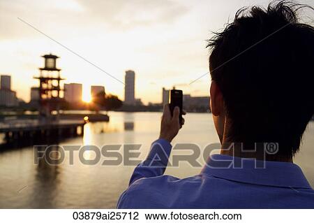 Stock Image - Back view of young man with mobile phone. Fotosearch