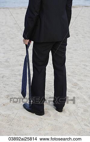 Businessman on beach, holding tie View Large Photo Image Picture - Businessman on beach, holding tie. Fotosearch
