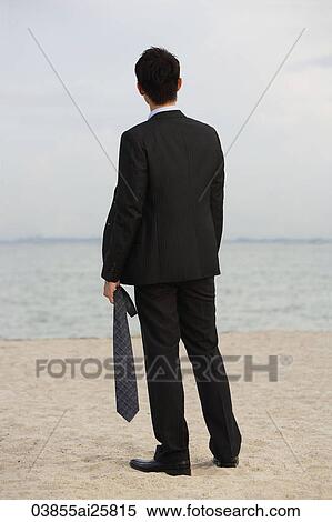 Businessman on beach, holding tie View Large Photo Image Stock Photography - Businessman on beach, holding tie. Fotosearch